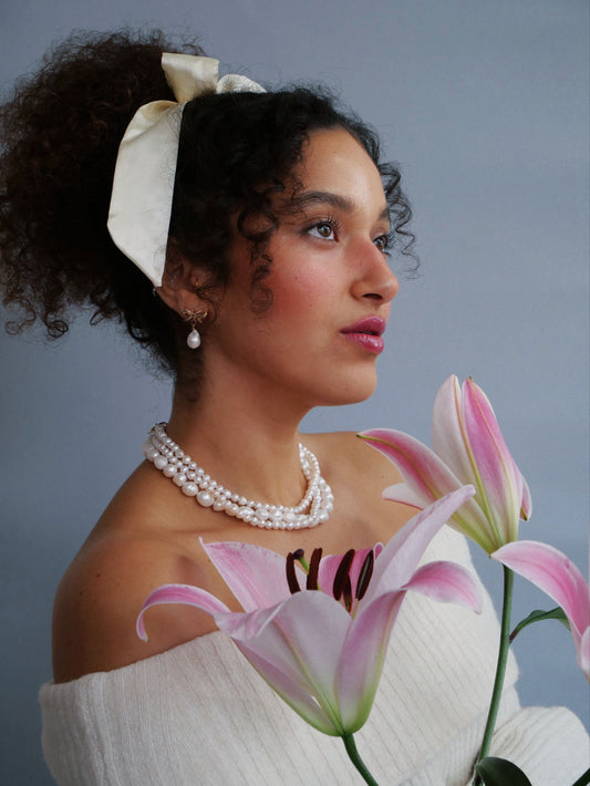 Curled hair model  white shirt white bow white pearl earrings 14K gold necklace pink lily flower